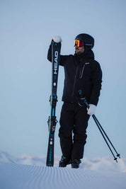 Person in ski gear holding skis and poles on a snowy landscape
