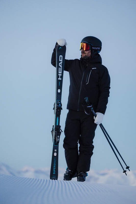 Person in ski gear holding skis and poles on a snowy landscape