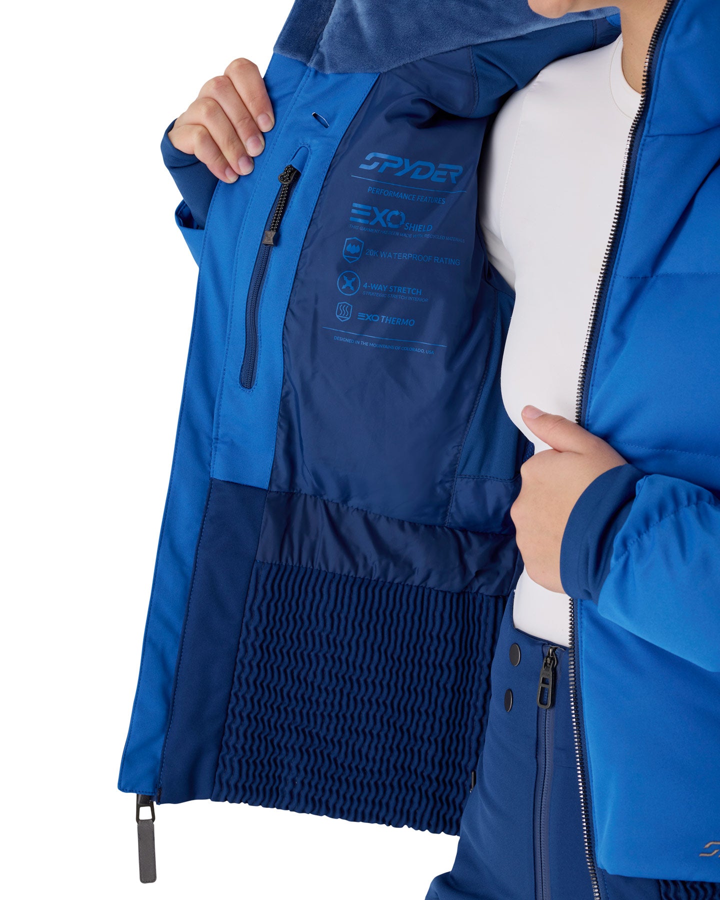 Close-up of a person wearing a blue Spyder ski jacket, opening the hood to reveal the interior lining with technical text and logos.